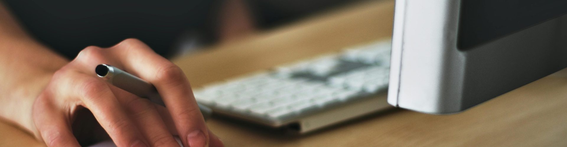 A hand using a wireless mouse at a modern desk setup with a computer and keyboard.